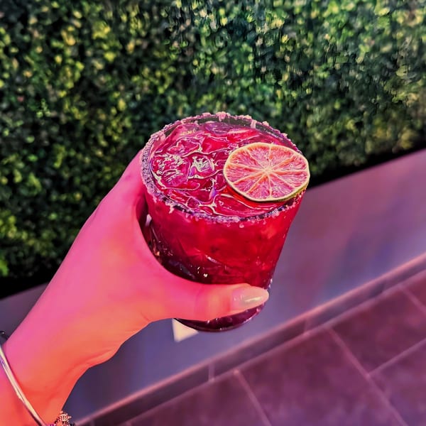 Hand holding a vibrant red Coco Mexican Restaurant margarita with a lime slice and salted rim.