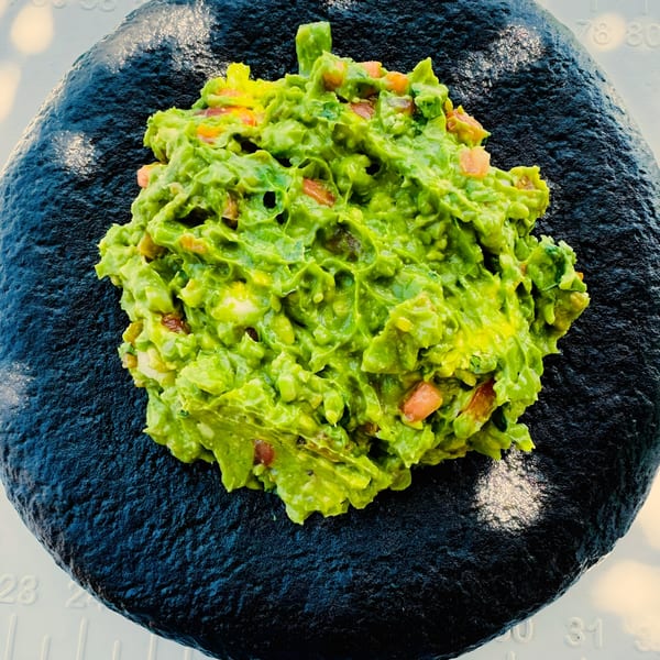 Freshly made guacamole with visible chunks of avocado and tomato, served on a dark, textured plate.