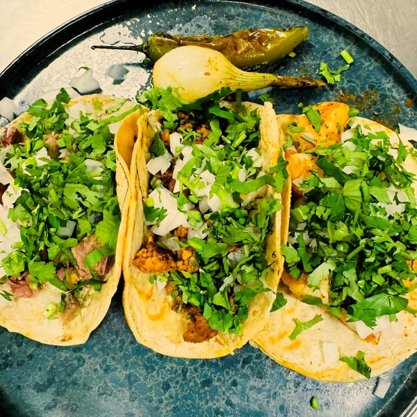 Three Coco Mexican Restaurant tacos with meat, cilantro, and onions, served with a grilled pepper and onion.
